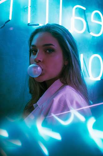 person selective focus photo of woman blowing gum standing in front of turned-on neon signage bubble
