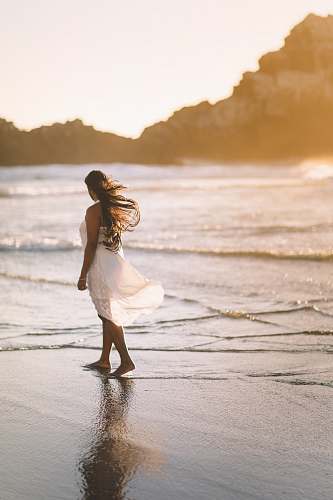 woman selective focus photo of woman standing on sea shore near rock formation during golden hour sea