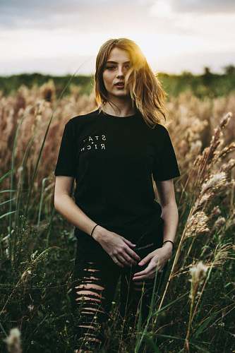 human selective focus photography of black crew-neck t-shirt and distressed black bottom standing on brown wheat field during daytime woman