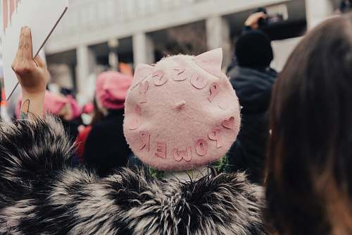 person selective focus photography of person wearing pink fleece Pussy Power cap raising right hand human