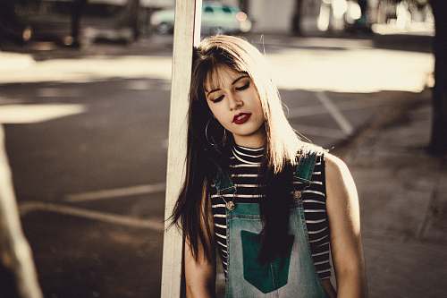 person shallow focus photography of woman leaning on brown wooden post woman
