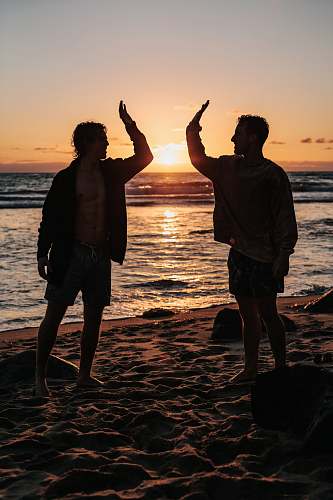 person silhouette of two mens near seashore about to high five during sunset human