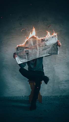 fire surrealism photography of person reading news paper in fire while sitting on stool flame