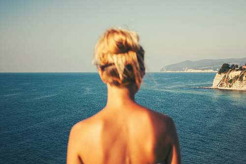 person topless woman standing facing blue sea under white sky beach