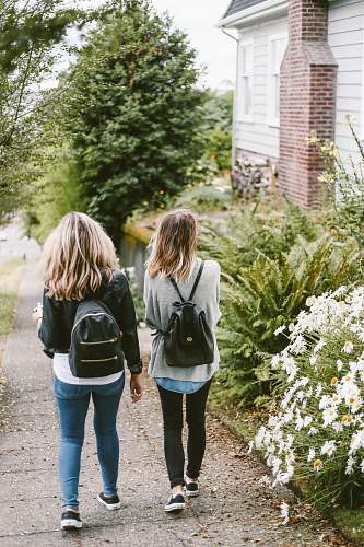 girl two ladies walking on sidewalk with black backpacks blonde
