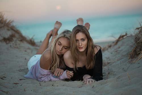 human two woman lying on sand facing camera woman