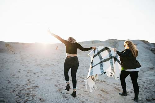 person vignette photography of two woman holding scarf walking on sand female