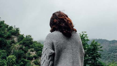 person woman in gray sweater standing in front of trees during daytime back