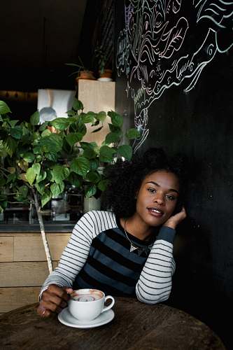 plant woman in white, black, and blue striped long-sleeved shirt sitting on chair in front of table holding white ceramic teacup flora