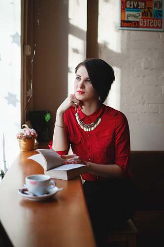 woman woman leaning on brown wooden table while holding book cup