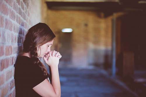 woman woman praying while leaning against brick wall girl