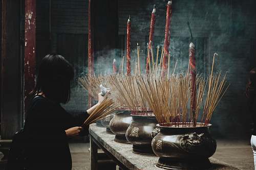 person woman putting incense sticks on pot incense