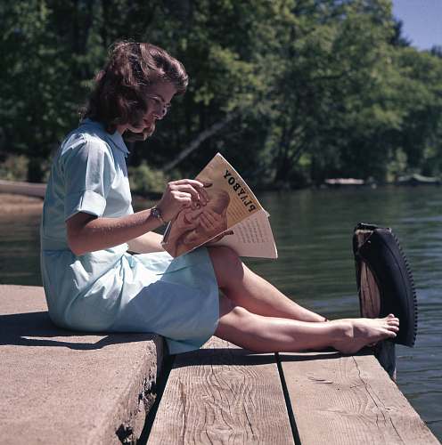 person woman sitting while reading near body of water vintage