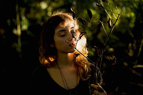 person woman wearing black necklace smelling plant during daytime woman