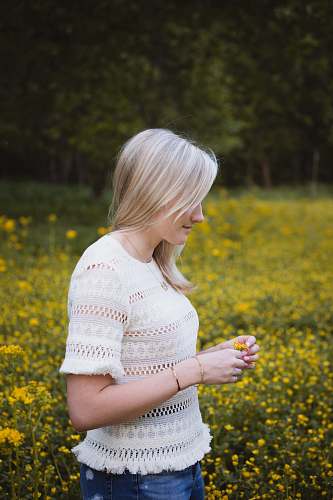 person woman wearing white blouse standing and holding yellow flower surrounded with flowers human