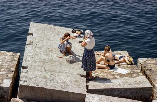 person Women in swimsuits and vintage clothing sunbathing on cement cubes by the sea human