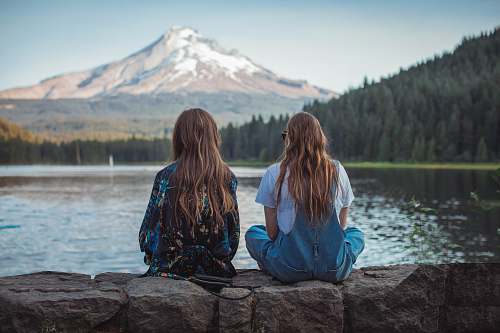 person women sitting on rock near body of water human