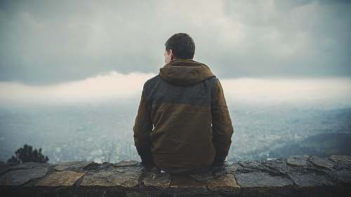 people man sitting on brown concrete surface while staring sideway human