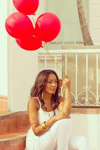 people woman sitting on staircase while holding red balloons woman