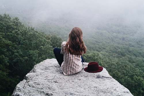 people woman sitting on top of gray rock woman