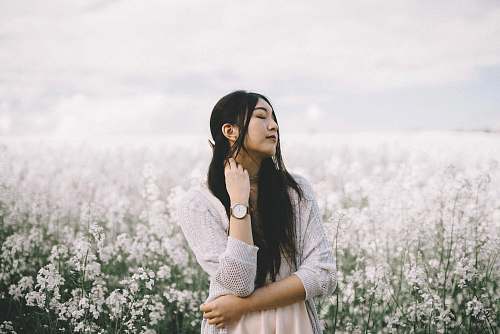 people woman wearing peach inner top with gray knitted cardigan standing behind white flowerfield during daytime photography woman