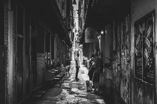 city grayscale photo of people in between of white concrete structures alley