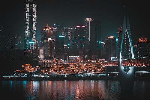 city body of water under bridge near buildings at night metropolis