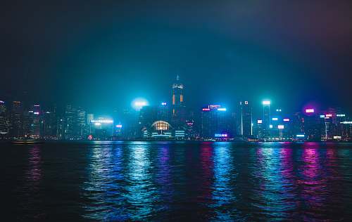 city lighted city buildings near body of water during nighttime metropolis