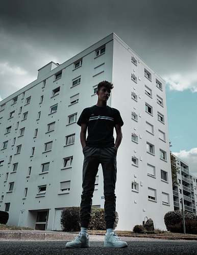 city low-angle photography of standing man with both hands in pocket during daytime high rise
