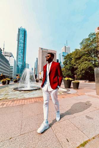 city man wearing red suit jacket and white pants walking on street downtown