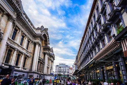 city people walking near brown historic buildings under white and blue sky during daytime downtown