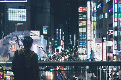 city person holding clear umbrella across city building during nighttime metropolis