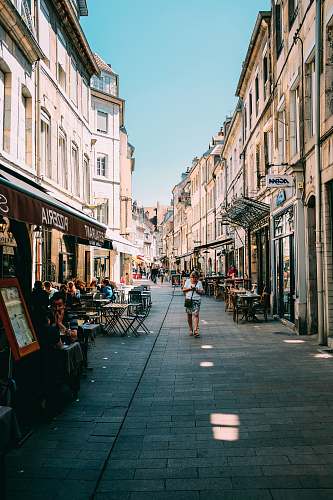 human person walking on alleyway with restaurant tables during daytime person