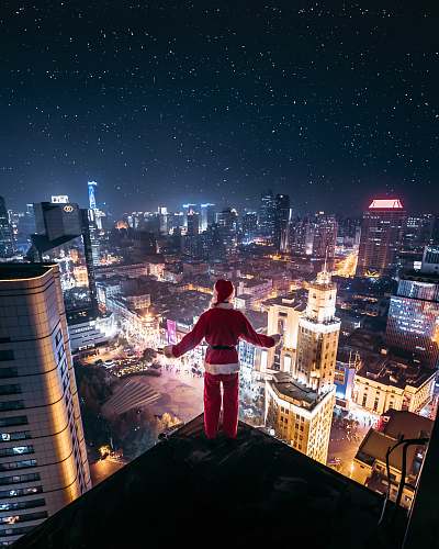 urban person wearing Santa Claus outfit standing on the edge of building at night time town
