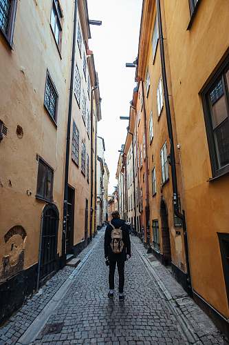 street man in black long-sleeved top and brown backpack walking on street alley
