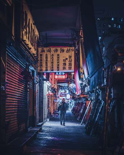 urban man in denim jacket and jeans walking on pathway near buildings at night street