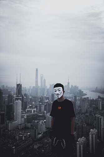 town man standing on top of building while wearing Guy Fawkes mask urban