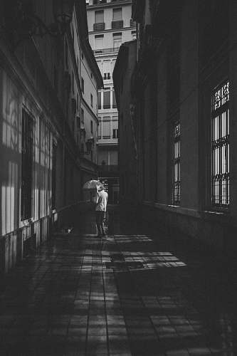 building person standing between alley black-and-white