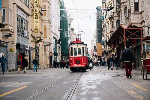 person red tram near between buildings with person walking during daytime people