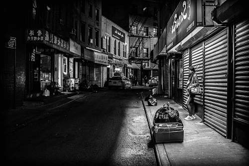 road grayscale photography of woman standing infront of store shutter door at night black-and-white