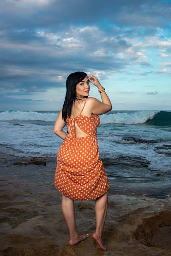 clothing standing woman in orange polka-dot spaghetti strap dress front of sea human