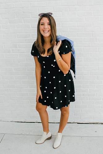 person woman in black and white polka dot dress standing beside white wall apparel
