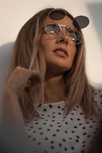 human woman in white and black polka dot shirt wearing silver framed aviator sunglasses person