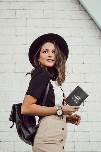 clothing woman in black blazer and brown dress holding booklet while looking into left side and smiling hat