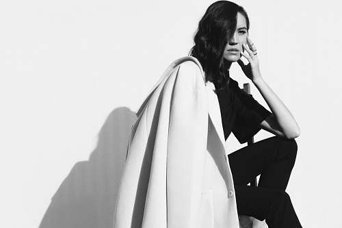 clothing grayscale photo of woman wearing t-shirt, pants, and with coat on left shoulder apparel