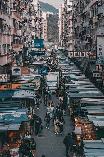 city aerial photography of people walking past display stalls between concrete buildings during daytime metropolis
