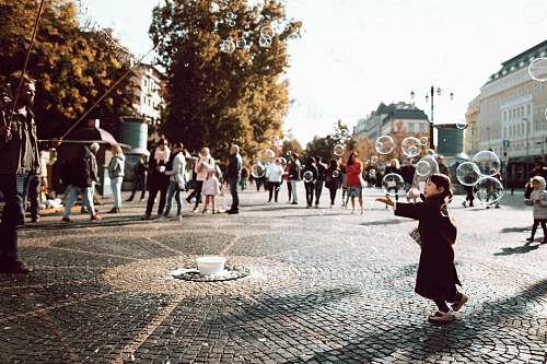 city girl in black coat trying to hold bubbles on air during daylight downtown