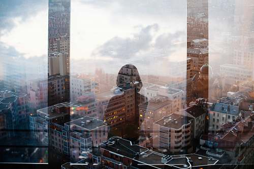urban reflection of woman standing in front of glass panel facing high-rise and mid-rise buildings building