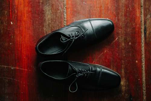 apparel pair of black leather lace-up dress shoes on brown wooden surface footwear