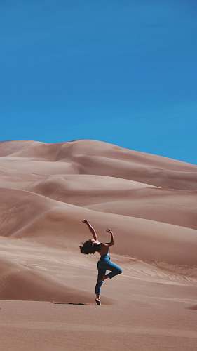 desert woman standing on right foot and raising hands at the bottom of sand dunes during daytime dance pose